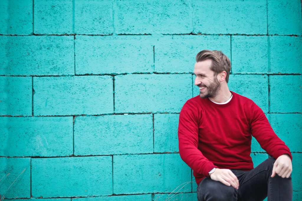 man wearing red sweatshirt and black pants leaning on the wall